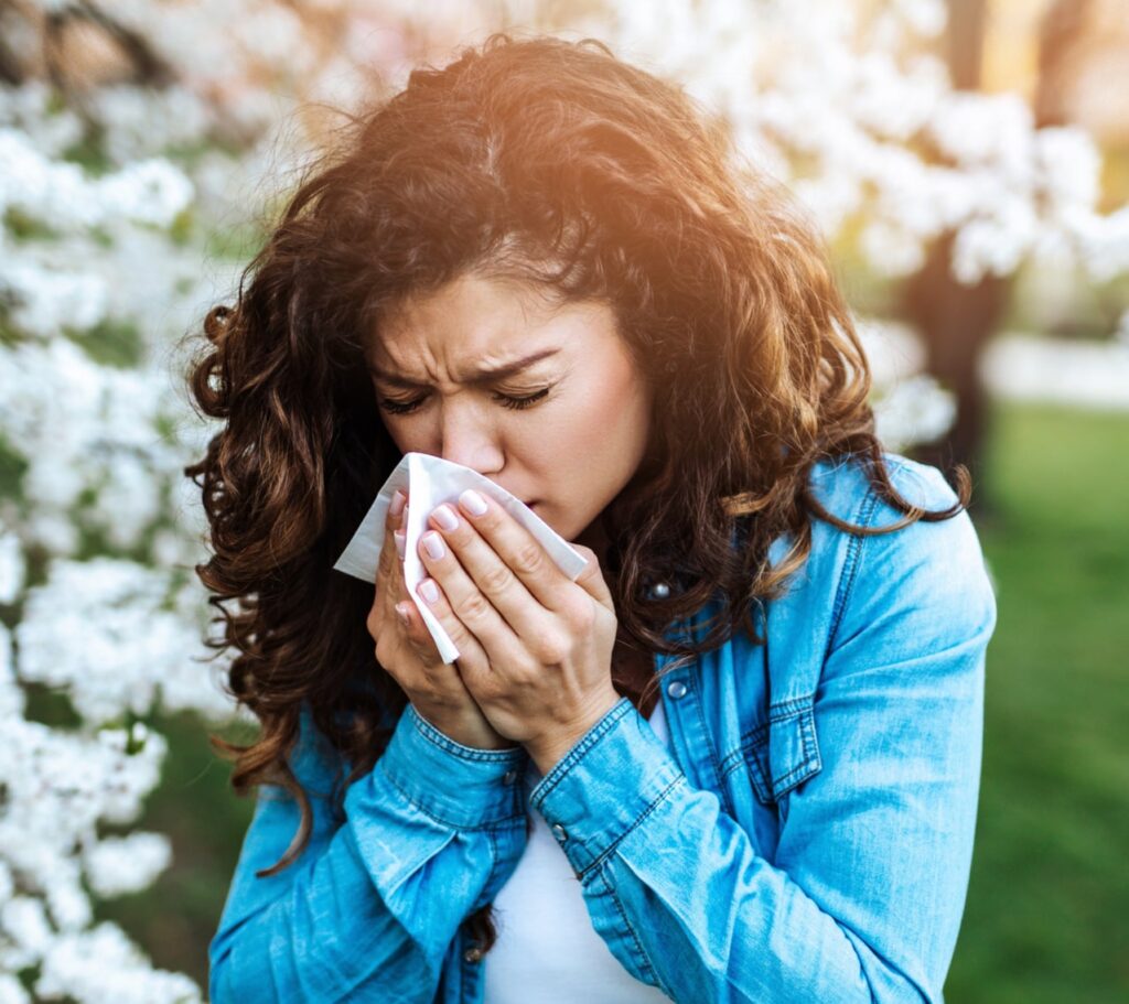 Young woman sneezing in park