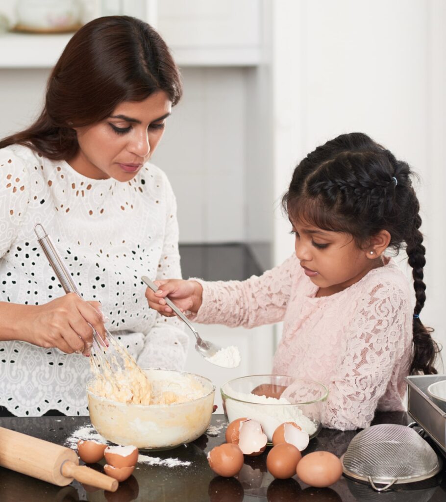 pretty little girl with two braids adding flour into bowl while cooking appetizing pie with mom